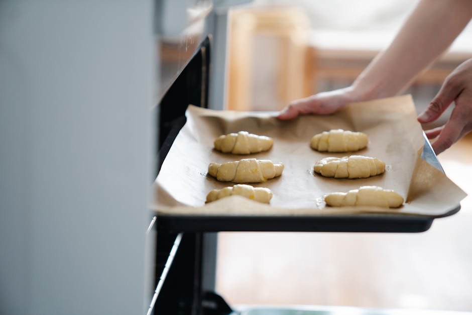 Freshly prepared croissants on a baking tray being placed into an oven.