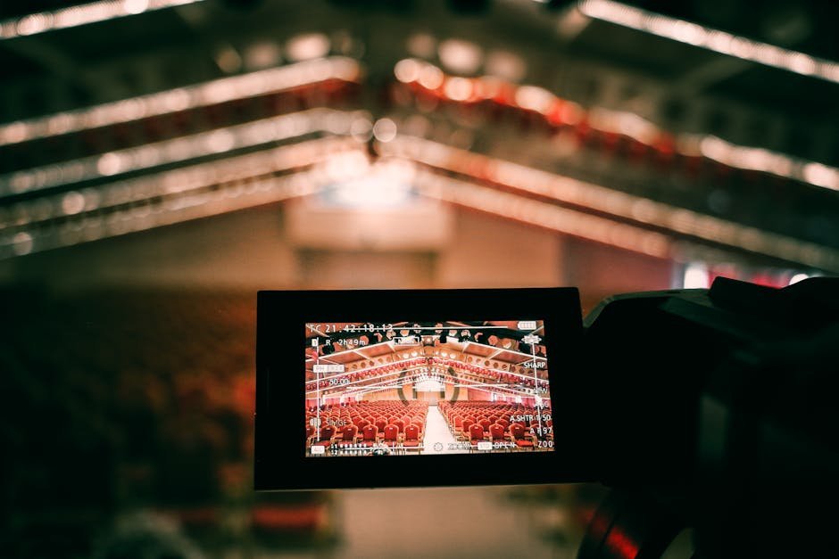 A digital camera screen captures an empty auditorium with rows of red seats under warm lighting.