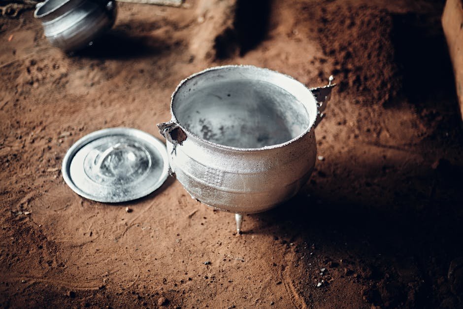 Vintage aluminum cooking pot with lid on rustic earthen floor, evoking traditional cookware.