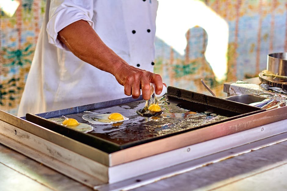 Chef prepares fried eggs on outdoor griddle, emphasizing culinary skill.