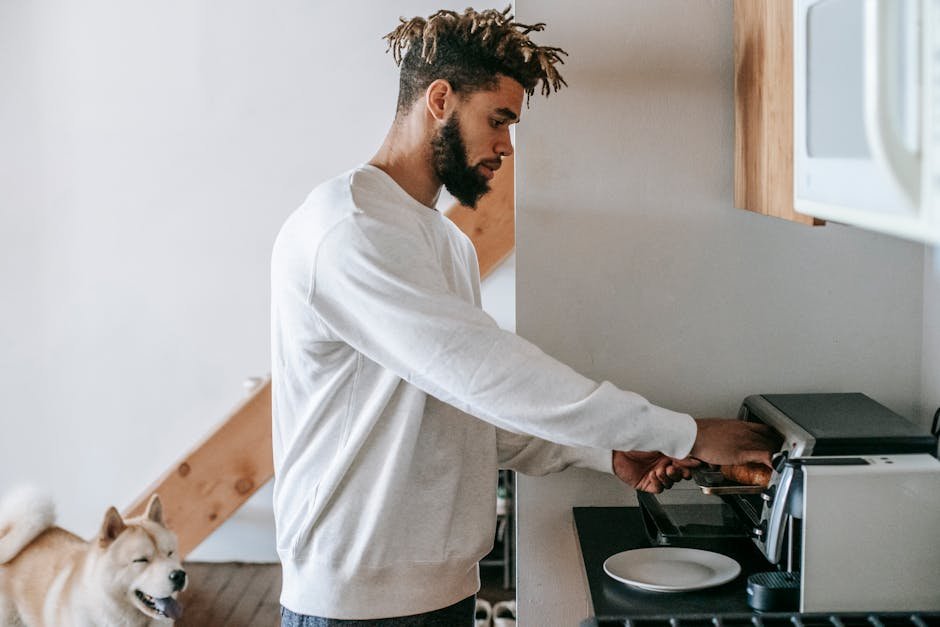 Young man using an oven toaster to prepare breakfast with his dog nearby in a cozy kitchen.