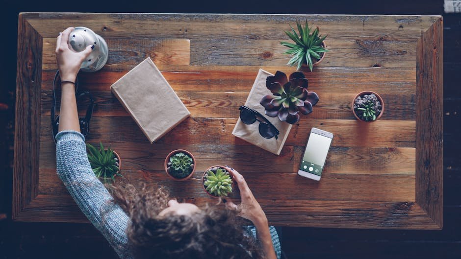 Overhead view of a cozy wooden table setup featuring plants, phone, and accessories.