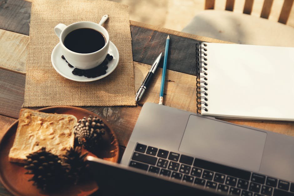 A warm, inviting workspace featuring a coffee cup, notebook, and laptop on a rustic table.