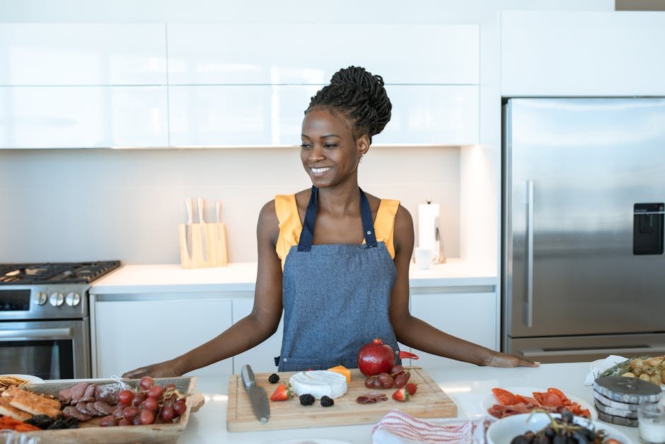 Smiling woman assembling a charcuterie board in a stylish kitchen setting with fresh and delicious ingredients.