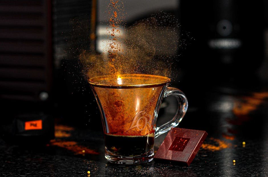 Close-up of coffee powder splashing above a shot glass with espresso, highlighting vibrant energy.