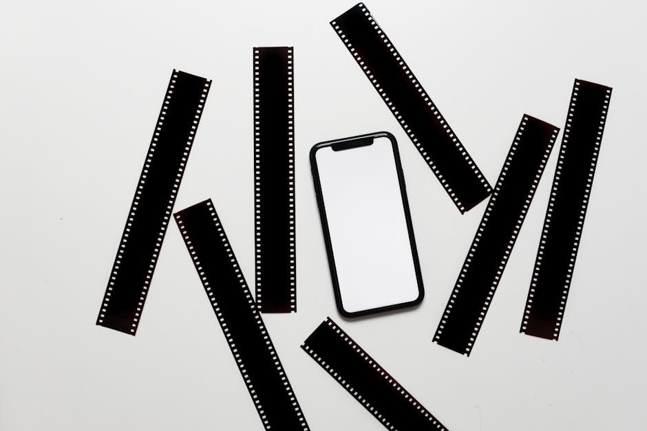 From above of retro photographic filmstrips scattered on white table near smartphone with empty screen