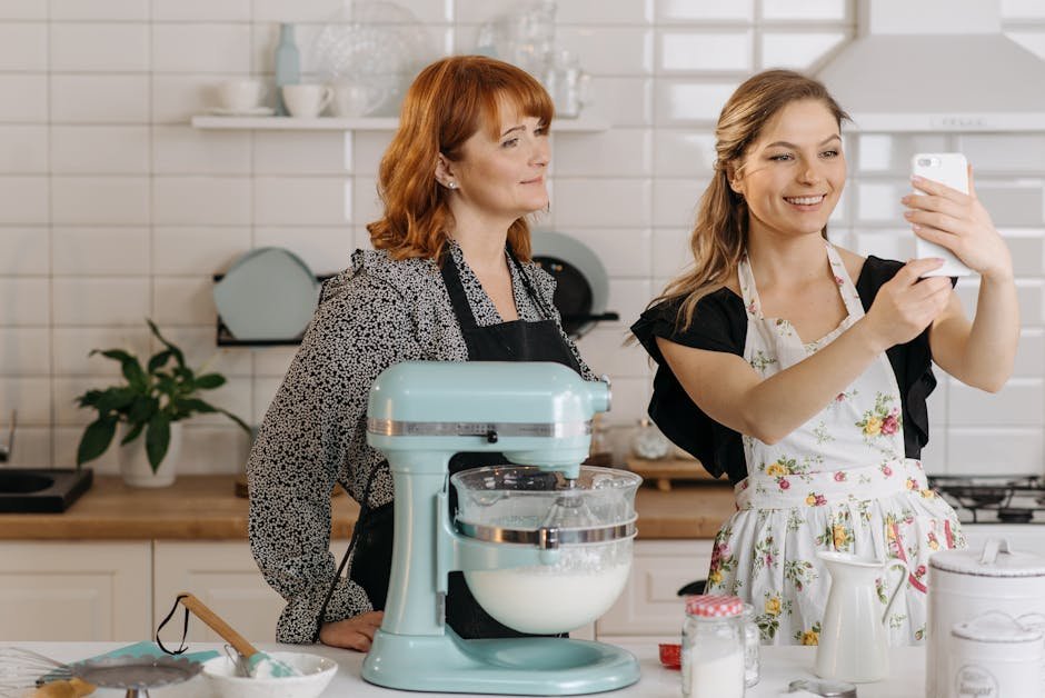 Two women in aprons taking a selfie while baking in the kitchen.