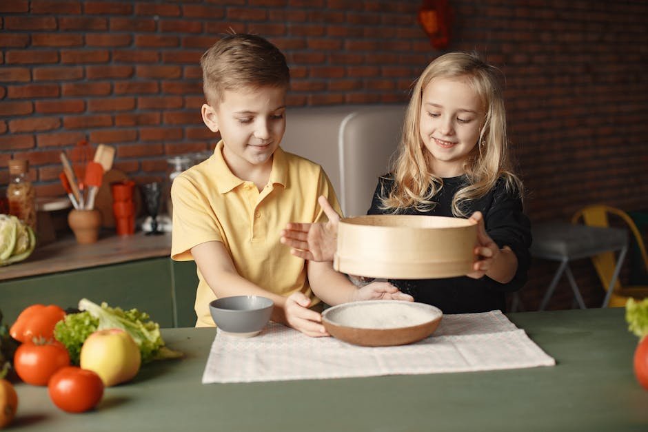 Content little friends in casual wear sifting flour through wooden sieve into round plate put on towel on table with fresh vegetables in loft style kitchen at home