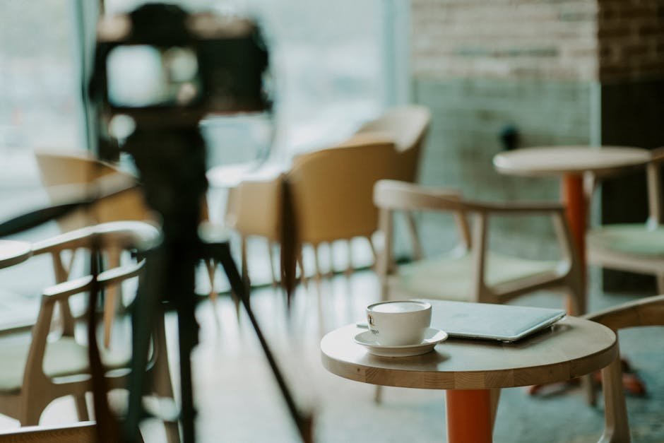 Warm café interior with coffee cup on table, laptop, and camera setup.